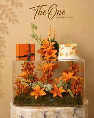 Luxury orange flower and cake arrangement with lilies and orchids in an acrylic display by The One Flowers UAE