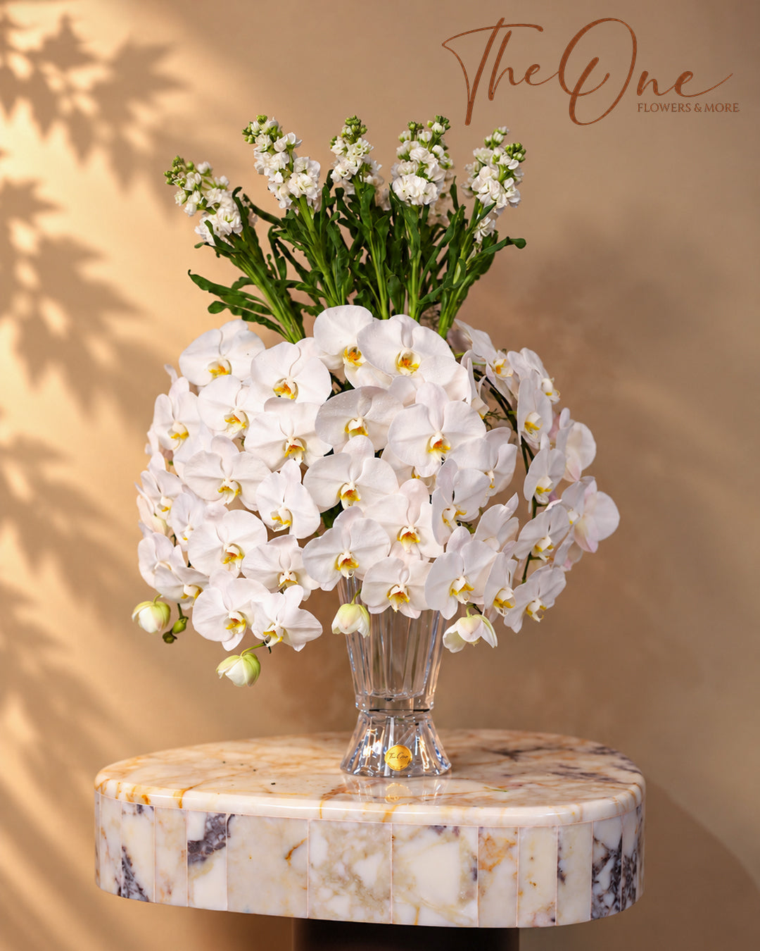 Luxury white Phalaenopsis orchid arrangement with elegant white flowers and green foliage in a clear glass vase by THE ONE FLOWERS, UAE.