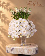 Luxury white Phalaenopsis orchid arrangement with elegant white flowers and green foliage in a clear glass vase by THE ONE FLOWERS, UAE.